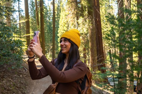 Woman wearing yellow beanie and brown top enjoying a hike in sequoia national park, filming tall