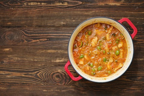 Pot filled with stew sits on wooden table. Stew has meat and green vegetables mixed together. Food