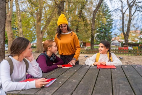 Mother and young daughters engaged in studying and learning together, sitting at a wooden picnic