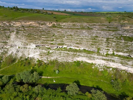 Steep cliffs with lush vegetation and a river course at the base in a green setting, aerial view,