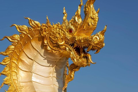 The golden Naga dragon rises against the clear sky of the Khao Kho Mountains. Its flame-like
