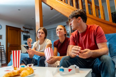 Family gathered on a blue sofa in a cozy living room, watching tv and streaming while sharing