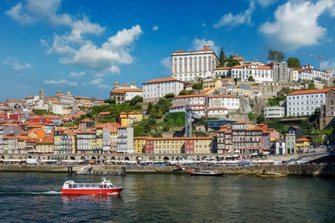 Red tourist boat on the Douro River in Porto, Portugal, passes Ribeira old town and its sunny