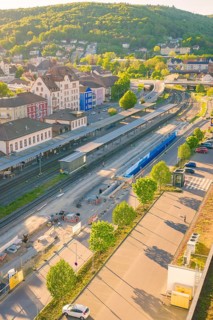 Railway station in sunshine, surrounded by dense vegetation and urban environment, electrification