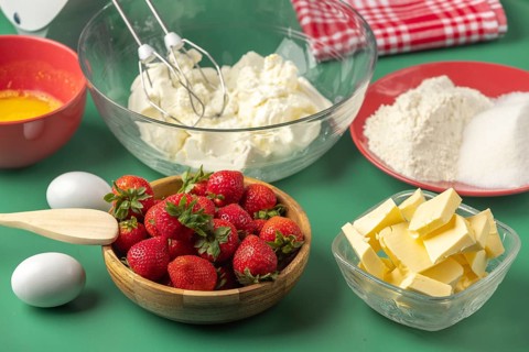 Fresh baking ingredients, including strawberries, butter, sugar and quark, on a green background