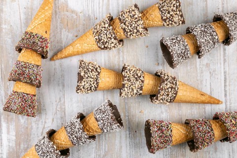 Ice cream cones decorated with nuts and sprinkles on rustic wood