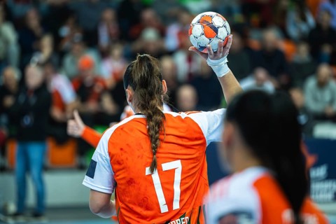 Female handball player wearing an orange jersey with number 17 holding the ball, ready to throw