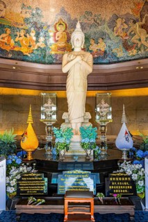 White Buddha statue in meditative posture in front of colorful wall mosaic and artfully designed