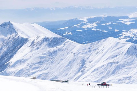 Red ratrac machine drives in Gidauri ski resort surounded by white high mountains.Gudauri.Georgia