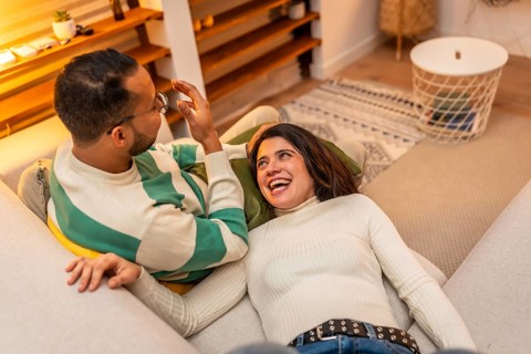 Young couple relaxing on a cozy living room sofa, laughing and enjoying an intimate, casual evening