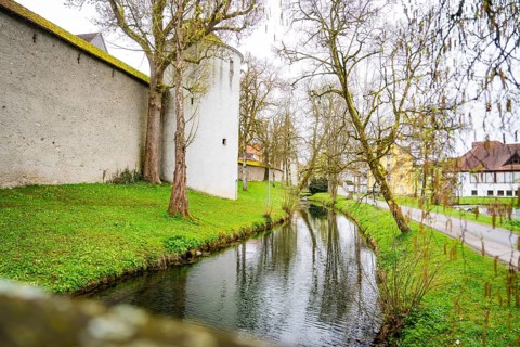 Small river along an old castle wall, surrounded by trees and green grass, Isny, Allgäu, Bavaria,