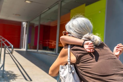 Grandmother and granddaughter sharing a loving hug outside a building with colorful windows,