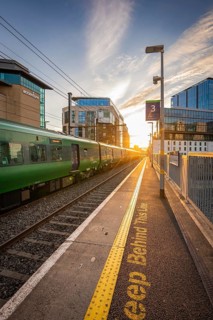 A green train stops at a platform as the sun sets between modern buildings, Dockland, Dublin,