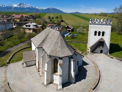 White tower and church in the village, with view of green fields and mountains on the horizon,