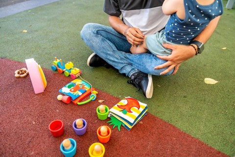 Father and child sitting on a colorful playground surface, interacting with a variety of colorful