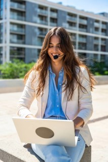 Smiling businesswoman wearing a headset, working remotely with her laptop in an urban outdoor