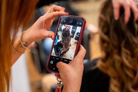 Hairdresser hands holding a smartphone, capturing content of a client's beautifully styled curled