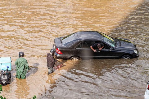 In a city affected by heavy rainfall, cars are submerged in water, and people are seen wading