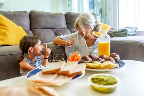 Grandmother and granddaughter enjoying a relaxed snack lunch together at home, sharing a special