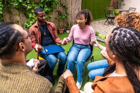 Diverse people participating in an outdoor group therapy session, sitting in a circle, holding