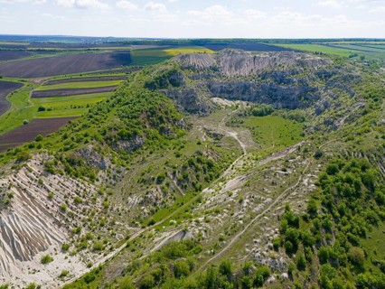 Extensive rocky landscape with green hills and isolated vegetation under blue sky, aerial view,