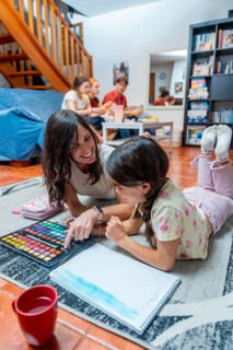 Mother and daughter paint with watercolors on the living room floor, smiling and bonding over