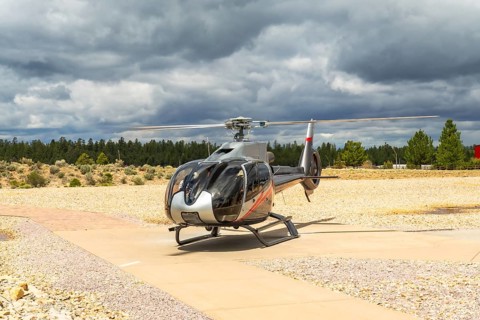 Helicopter parked on an asphalt helipad, preparing for scenic flying tours, with a dark cloudy sky