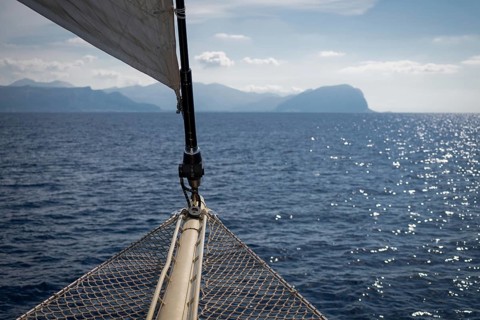 View over the bow net or safety net of a sailboat of the Mediterranean Sea and the Sicilian coast