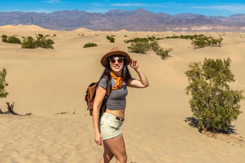 Woman standing on mesquite flat sand dunes in death valley national park, wearing hat and backpack,