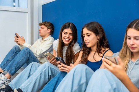 Young diverse students sitting on the floor, some laughing, while interacting and absorbed by their