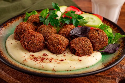 A plate holds falafel balls, tahini, salad with tomatoes and cucumbers, and a drink. The setting is