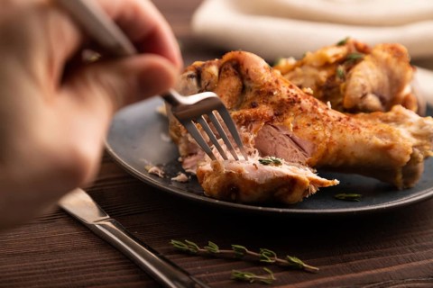 Fried Turkey Wing with spices and thyme on plate with hand on brown wooden background and linen