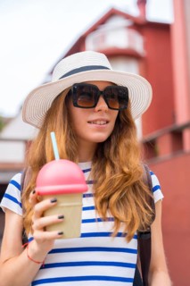 Young woman smiling and holding a novelty ice cream cone shaped cup with a straw, wearing a striped