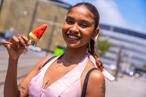 Young woman enjoying a refreshing watermelon popsicle on a sunny day, smiling confidently while