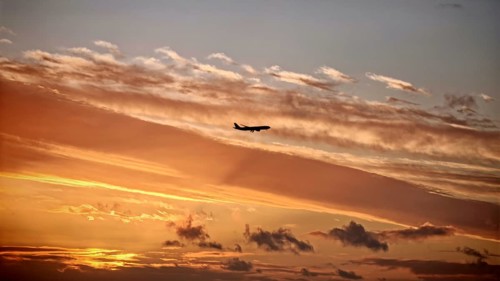 An airplane flies through a dramatically colored sunset sky, Lisbon, Portugal, Miradouro da Senhora