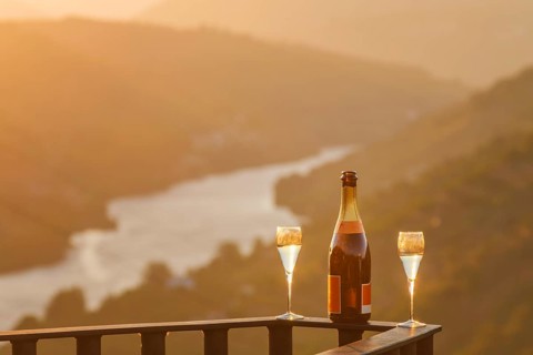Bottle of sparkling wine and two glasses on a terrace railing with the Douro River glowing in soft