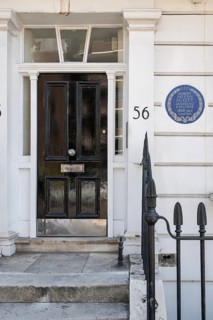 Entrance with black door and blue sticker on white house wall reminding that Robert Falcon Scott,
