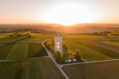 Sunset over fields with water tower and wind turbine, peaceful and wide landscape in warm light,