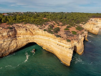 Drone view of Benagil Cave cliffs in Algarve, Portugal, with a tourist tour boat near the sea cave,