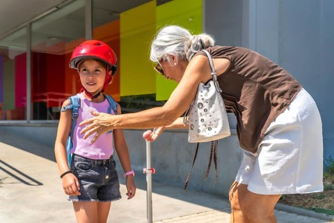 Grandmother bending down while picking up her granddaughter carrying a backpack and wearing a