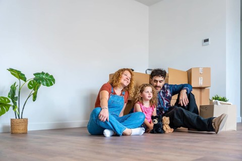 Happy family with parents and daughter sitting on floor in empty living room, surrounded by