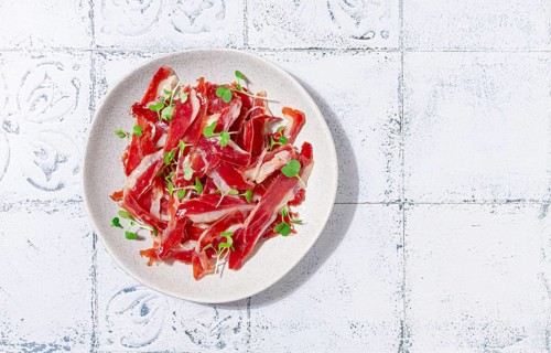 Ham of duck breast, dried duck fillet, with microgreens, plate, on a tiled table