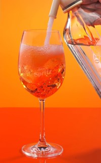 Aperol Spritz against an orange background is topped up with soda water