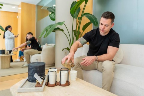 Man pouring water into disposable cups for a patient in a bright, contemporary aesthetic clinic