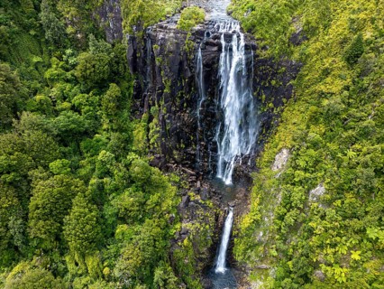 Stunning aerial photo of a tall waterfall flowing down dark volcanic rock surrounded by lush green