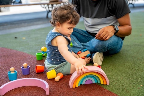 Young child creating a rainbow arch with educational wooden blocks while father watches, enjoying a