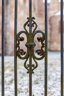 Close-up of an ornate, rusty iron fence on a cold winter day with snow-covered ground, iron grid at