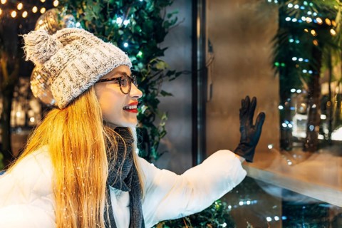 Happy young woman in winter clothing looking at store window display. A woman wearing a white