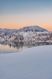 Dawn and sunrise at the wintry Forggensee in a snow-covered winter landscape in the foothills of
