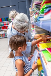 Grandmother and granddaughter are selecting colorful notebooks from a store shelf, preparing for